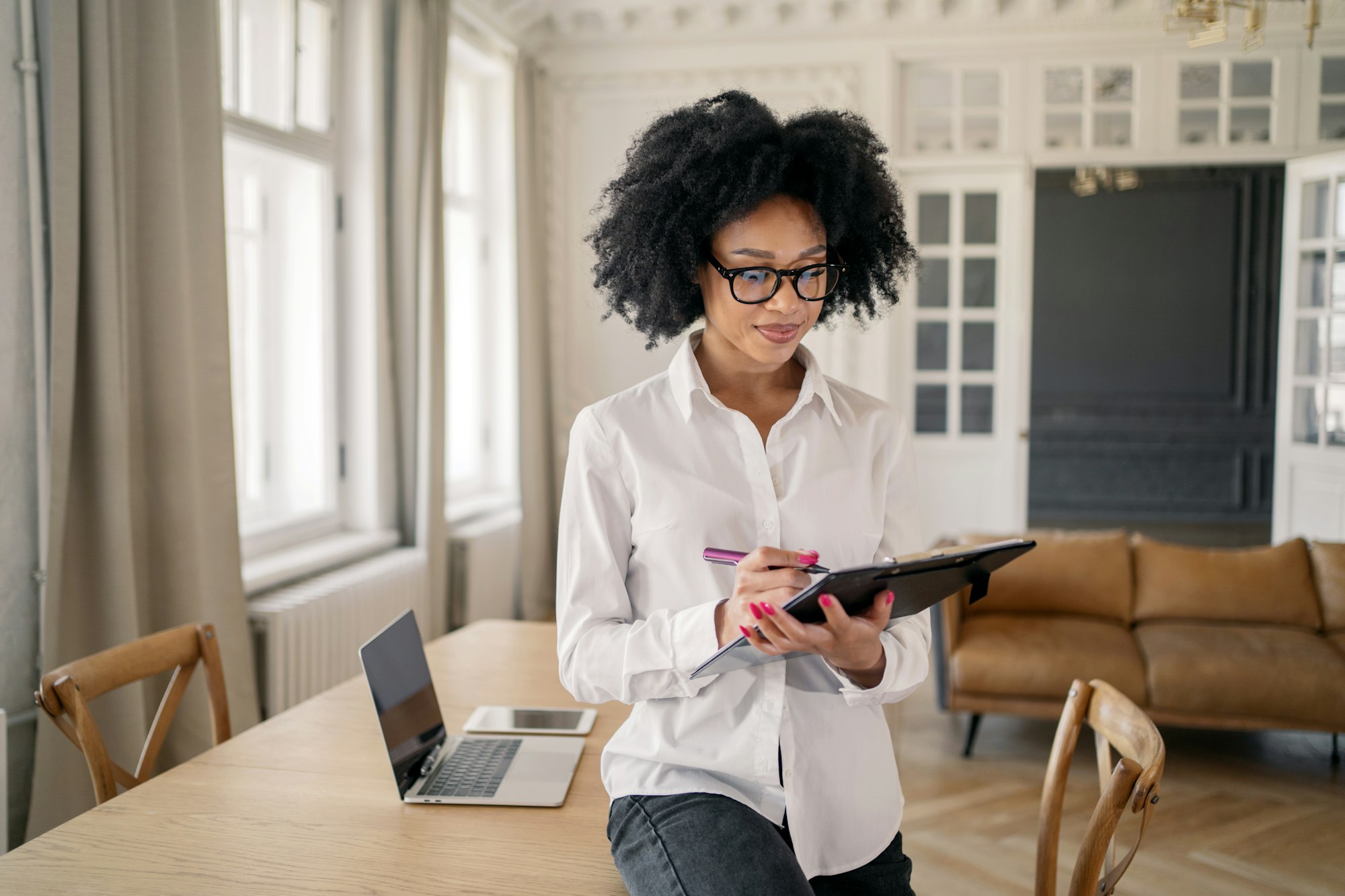 A young woman in an office in a white shirt uses a tablet for analytics records data.